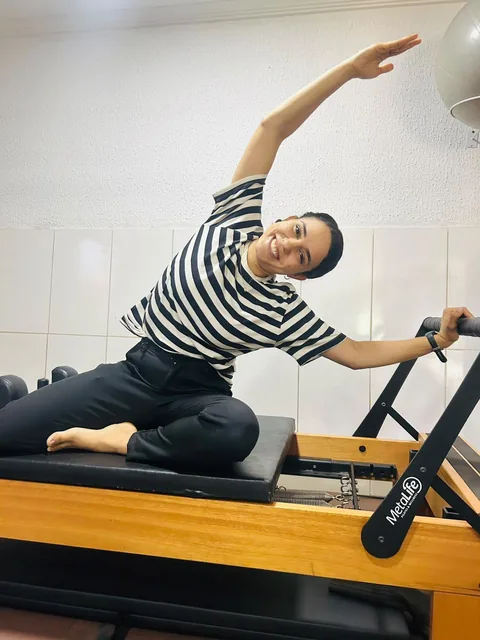 Leticia realizando um alongamento lateral no equipamento de Pilates.