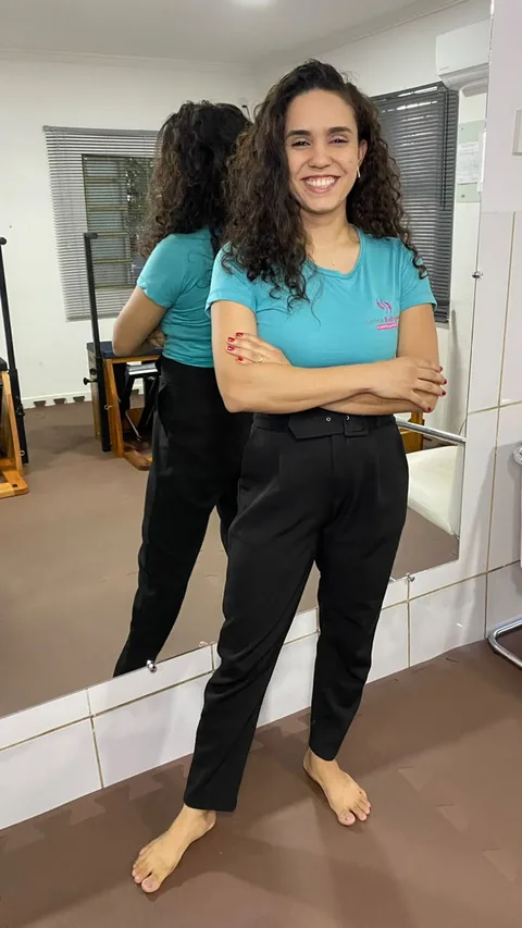 Leticia no estúdio, de camiseta turquesa, em frente ao espelho.