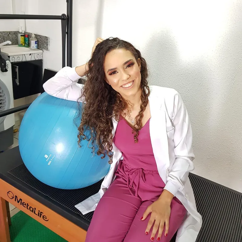 Dr. Leticia R. Cavalcante sorrindo no estúdio, ao lado de uma bola de Pilates.